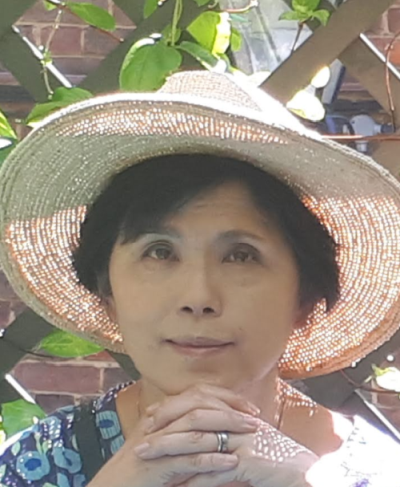 Portrait photo of Kumi smiling, wearing a sun hat.